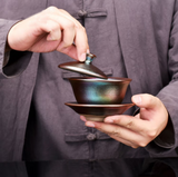 Person brewing tea in a metallic rainbow gaiwan